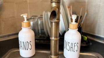 A kitchen sink with two soap dispensers labeled 'HANDS' and 'DISHES' and a dish rack in the background.