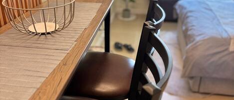 A dining area with a wooden table, two leather chairs, a metal wire basket, and a television in the background.