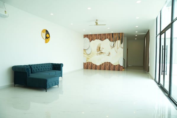 A spacious room with a modern design, featuring a blue sofa, a wall mural, and a ceiling fan.