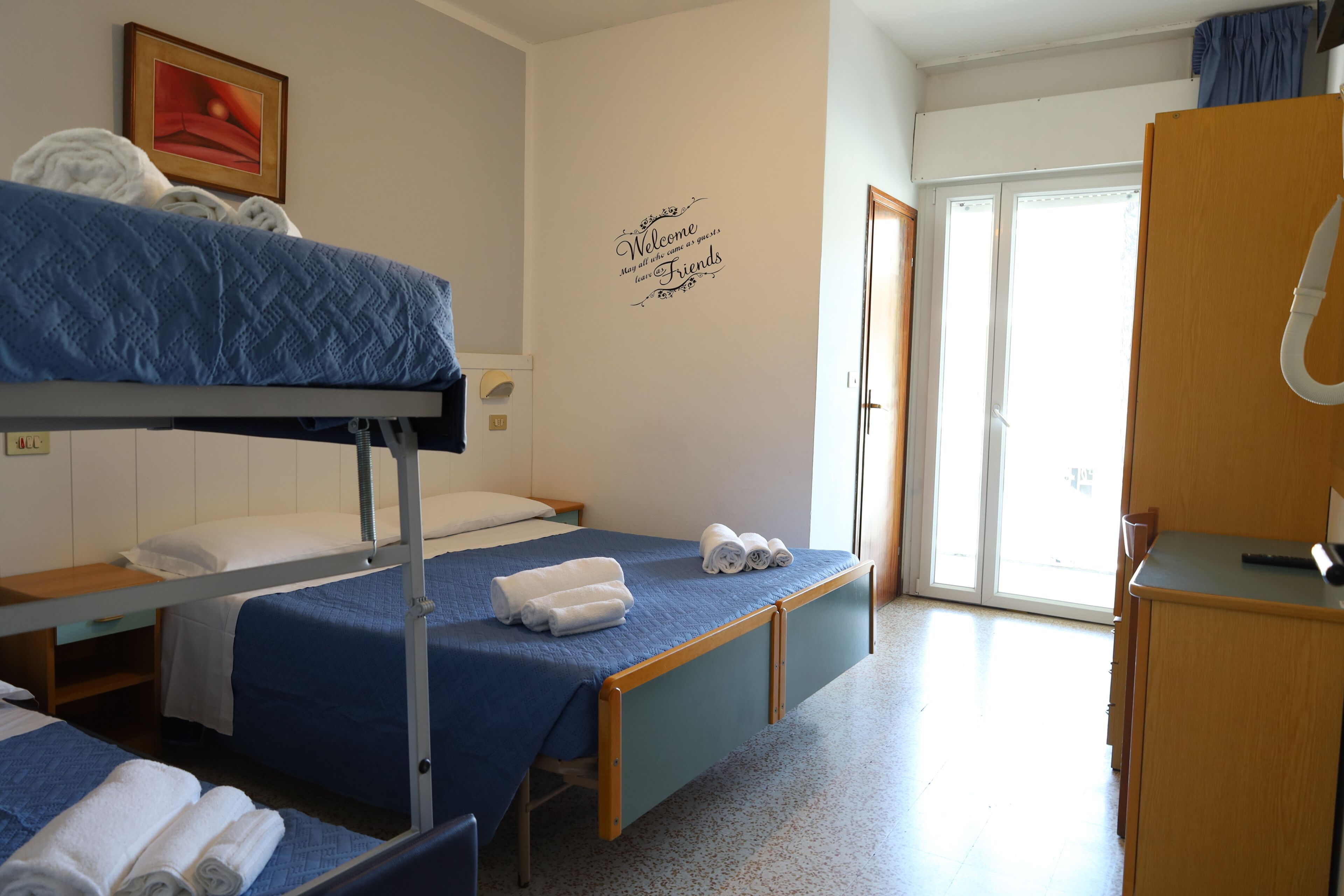 A hotel room with bunk beds, a desk, a wardrobe, and a sliding door to the outside.
