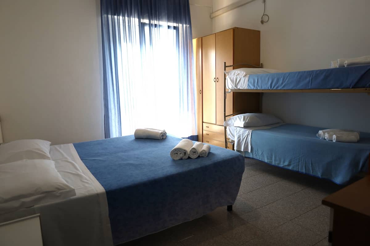 Ein Hotelzimmer mit einem Einzelbett, einem Etagenbett, einem Kleiderschrank und einem Fenster mit Vorhängen.