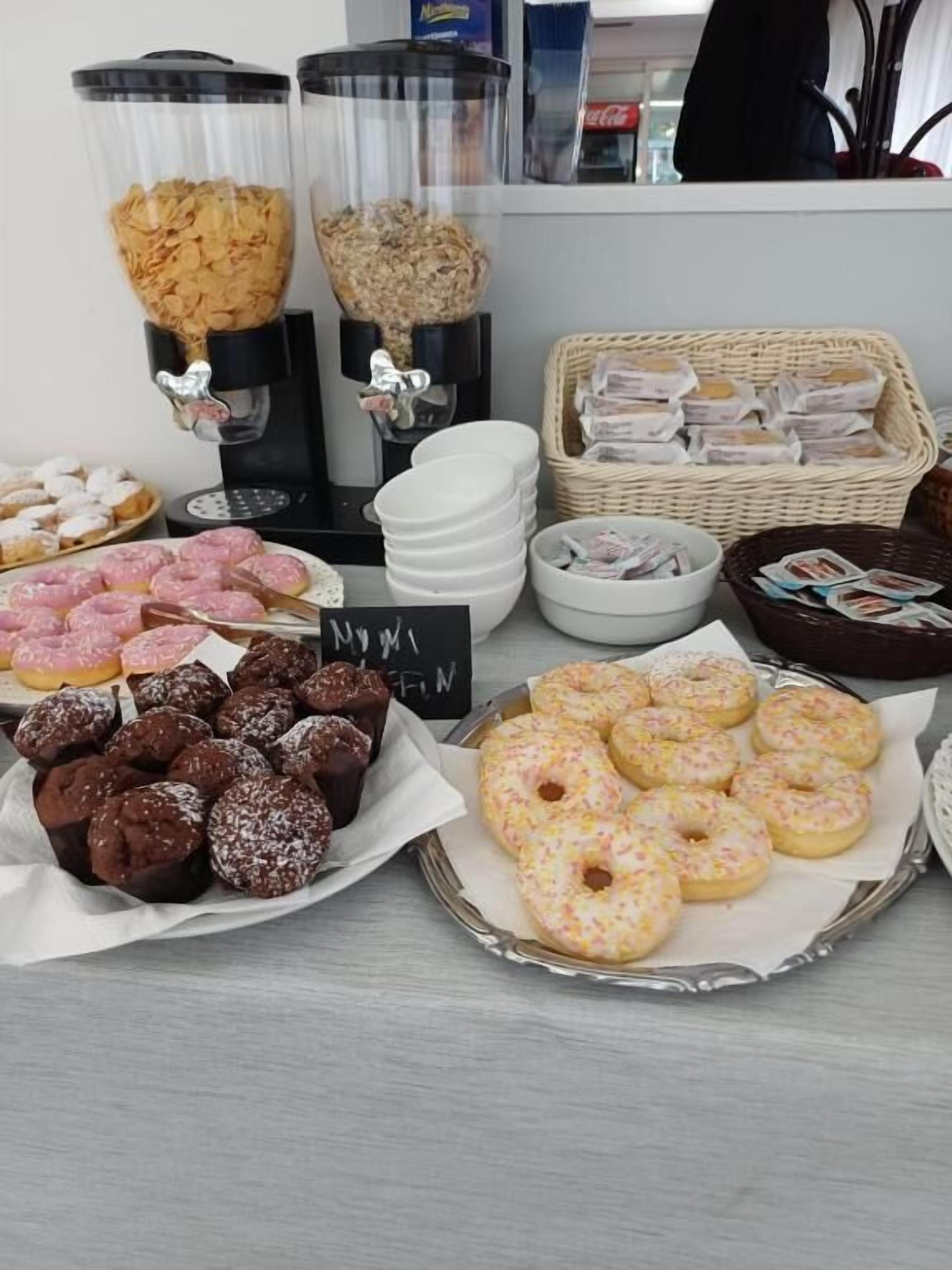 Un tavolo del buffet con diversi cibi, tra cui ciambelle e pasticcini, e una macchina per il caffè.