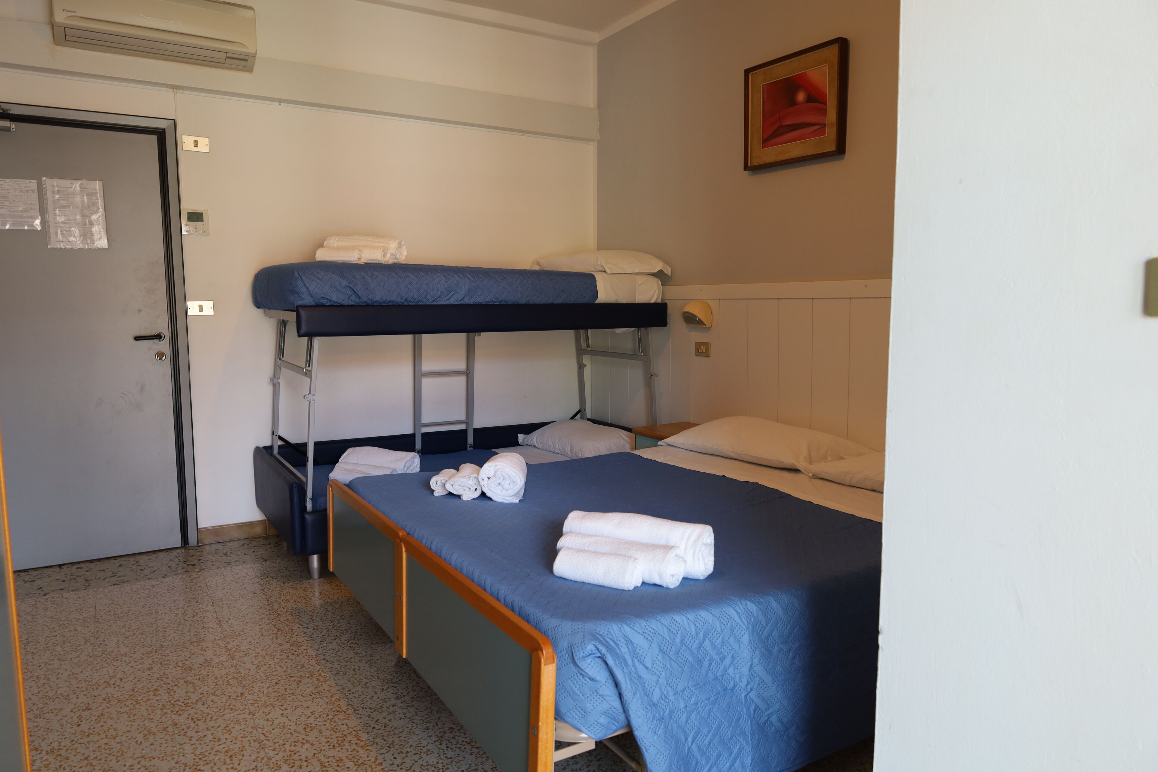 A bunk bed room with a door, a framed picture on the wall, and a bed with rolled towels.