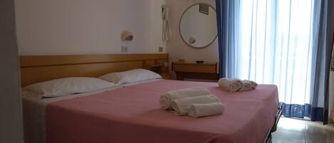 A hotel room with a bed, a bedside table, a mirror, and a window with curtains.