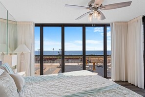A bedroom with a large bed, a ceiling fan, and a view of the beach through large windows. - Golden Sands 104 by Seaside Vacations & Sales (Ocean City)