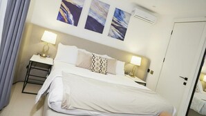 Hotelkamer met een bed, twee nachtkastjes, een lamp, een airconditioner en drie abstracte schilderijen aan de muur.