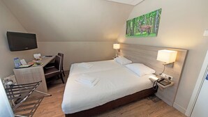 Ein Hotelzimmer mit Bett, Schreibtisch, Stuhl, Fernseher und einem Bild an der Wand.