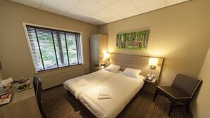 Una camera d'albergo con un letto grande, due comodini con lampade, una scrivania con una sedia, un termosifone e una finestra con tende.