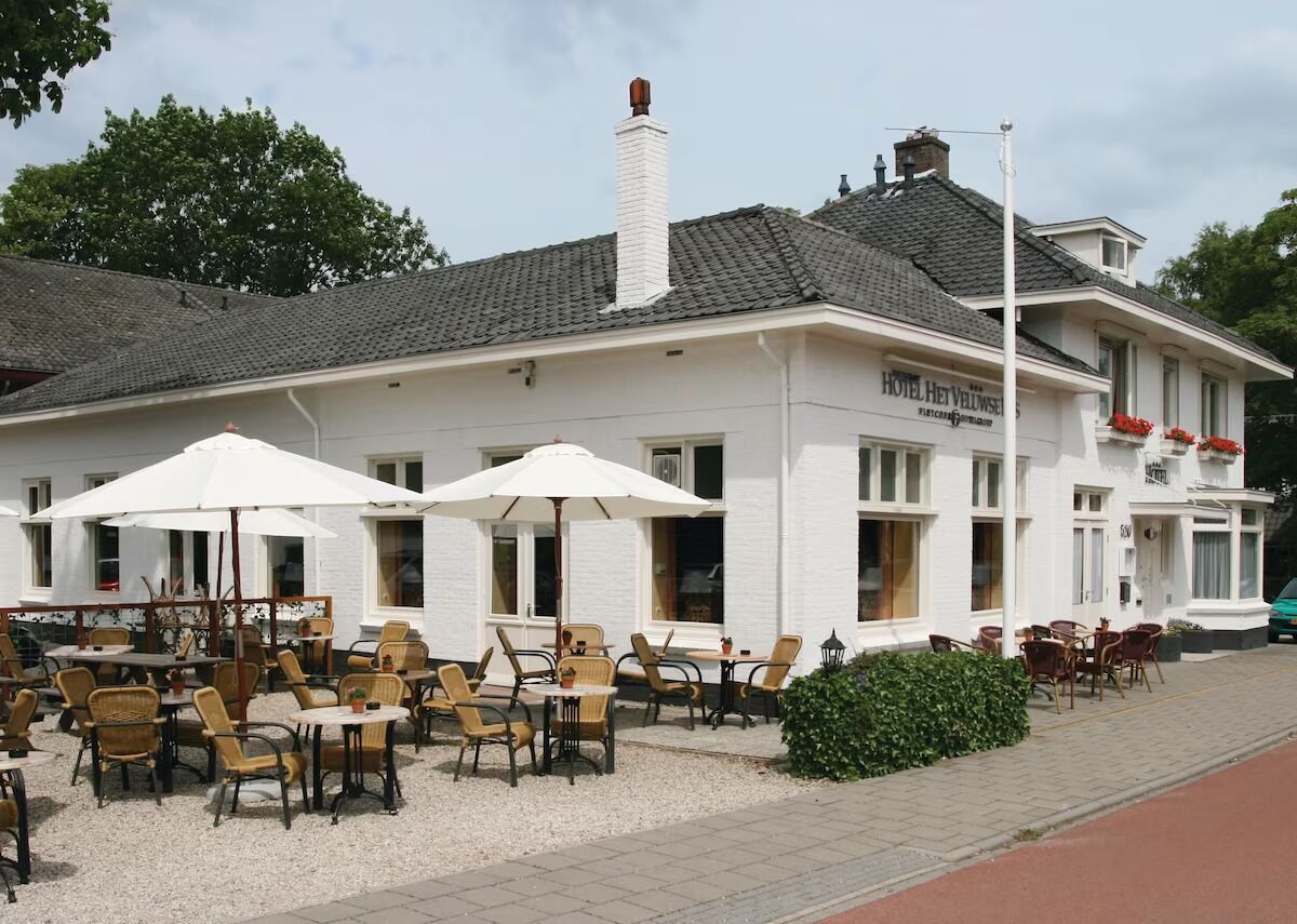 A hotel with outdoor seating, a white facade, and a chimney.