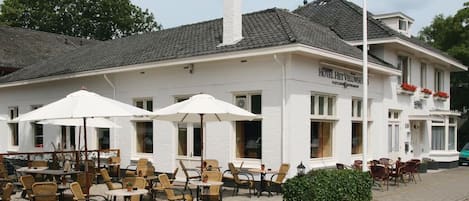 A hotel with outdoor seating, a white facade, and a chimney.