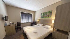Une chambre d’hôtel avec un grand lit, un bureau avec une chaise, une télévision, une fenêtre avec des stores et un tableau représentant un cerf accroché au mur.