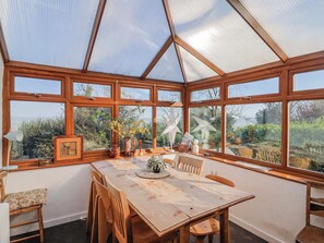 Ein Wintergarten mit einem Holztisch und Stühlen, großen Fenstern und Blick auf Grünflächen.