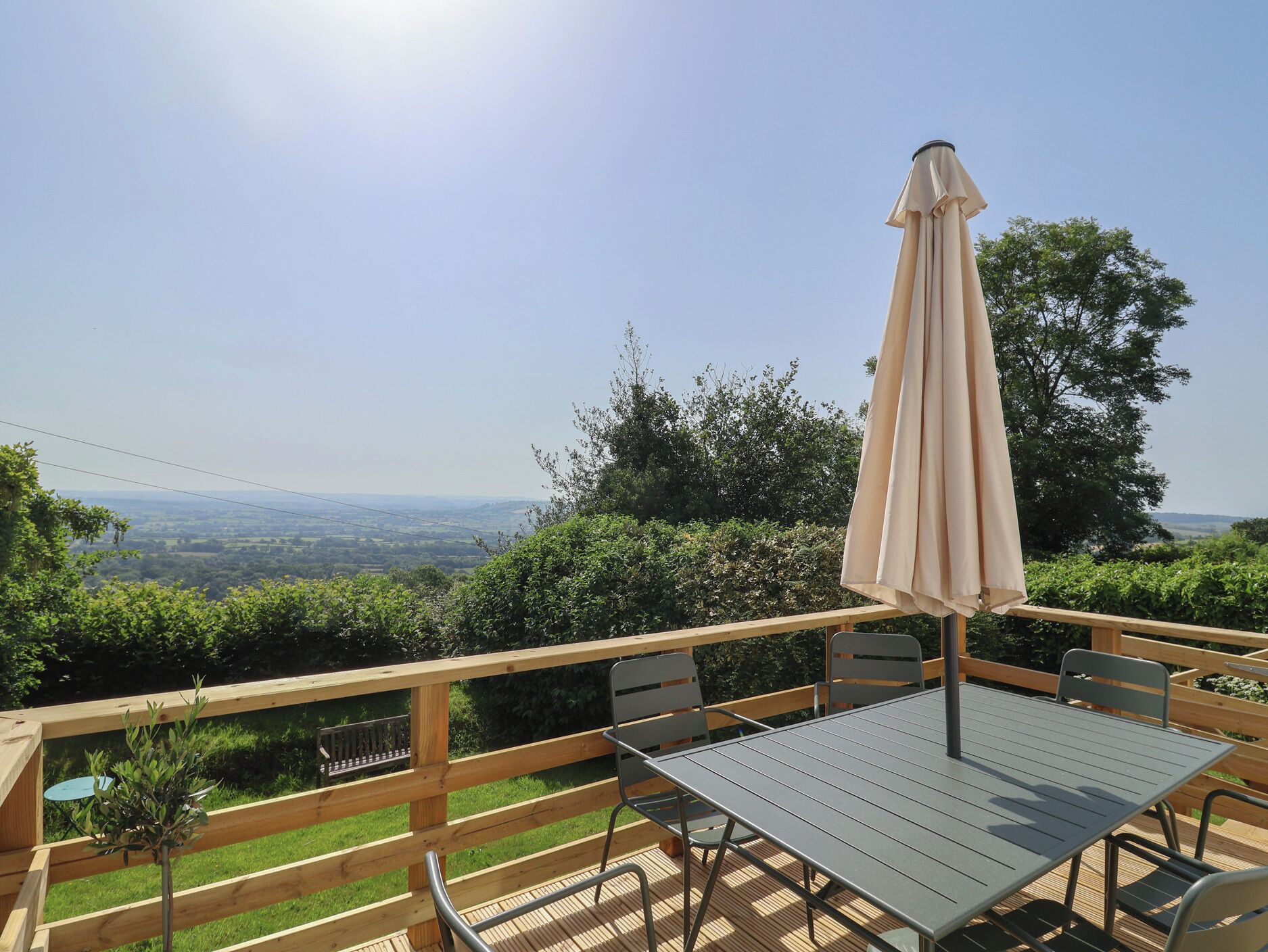 A wooden deck with a table and chairs, an umbrella, and a view of the countryside.
