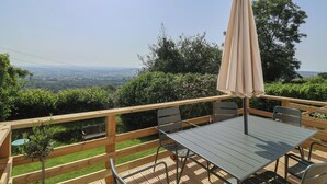 A wooden deck with a table and chairs, an umbrella, and a view of the countryside. - 2 Oak Tree Cottages (Axminster)