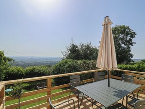 Eine Holzterrasse mit Tisch und Stühlen, einem Sonnenschirm und Blick auf die Landschaft.