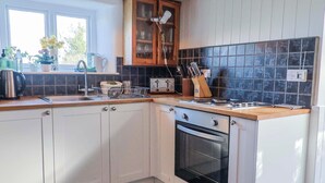 A kitchen with white cabinets, a black oven, a wooden countertop, and a tiled backsplash. - 2 Oak Tree Cottages (Axminster)
