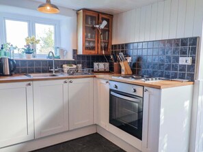 Eine Küche mit weißen Schränken, einem schwarzen Backofen, einer Holz Arbeitsplatte und einer gefliesten Rückwand.
