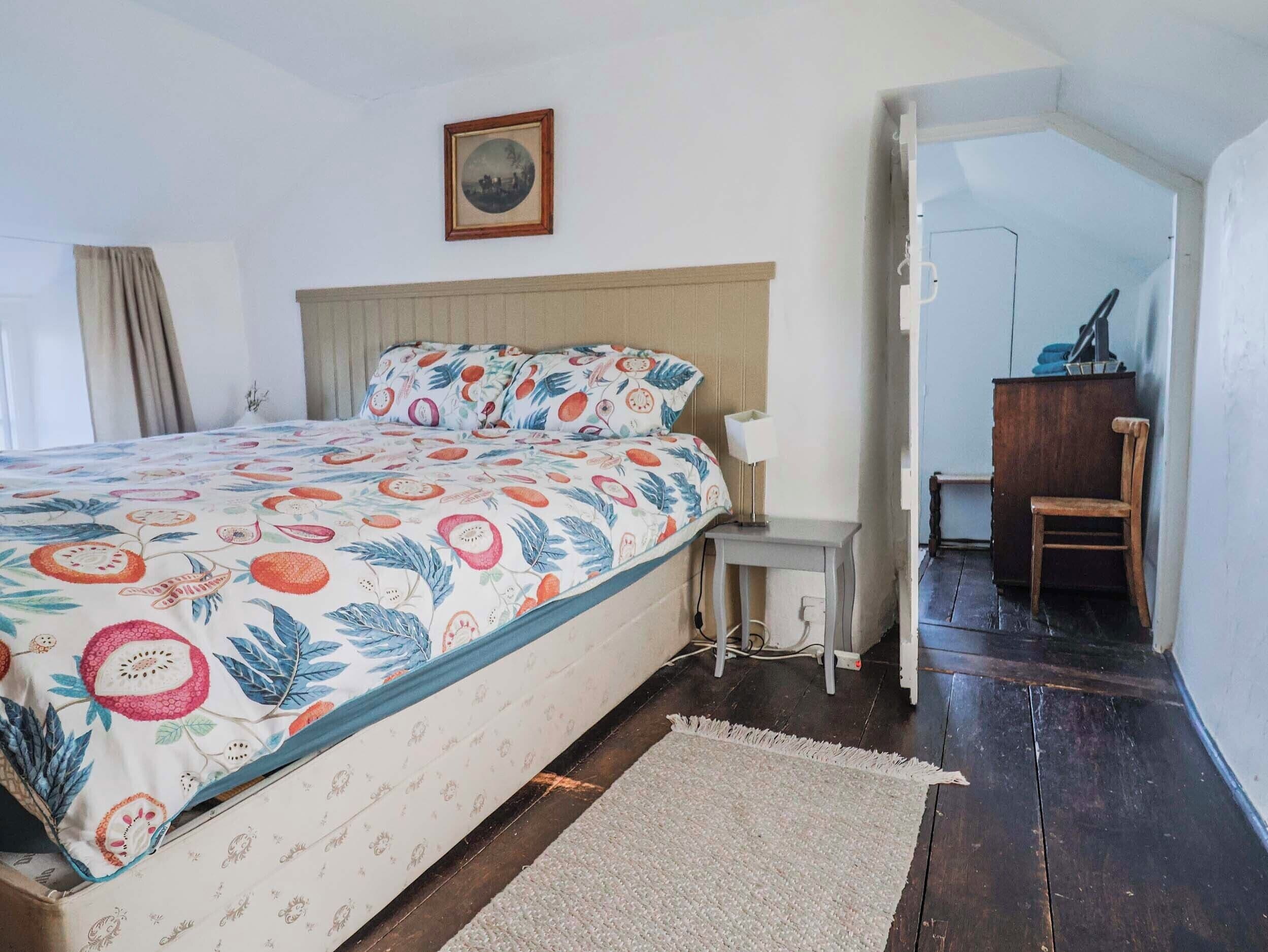 A bedroom with a bed, a bedside table, a chair, a desk, and a picture on the wall.