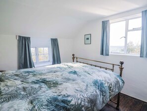 A bedroom with a bed, a window with curtains, a framed picture on the wall, and a view of the outdoors. - 2 Oak Tree Cottages (Axminster)