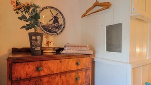 A wooden dresser with drawers, a vase with flowers, a plate with a windmill design, and a wooden hanger on the wall. - 2 Oak Tree Cottages (Axminster)