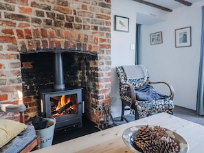 A rustic room with a brick fireplace, a wooden chair, and a table with pine cones. - 2 Oak Tree Cottages (Axminster)