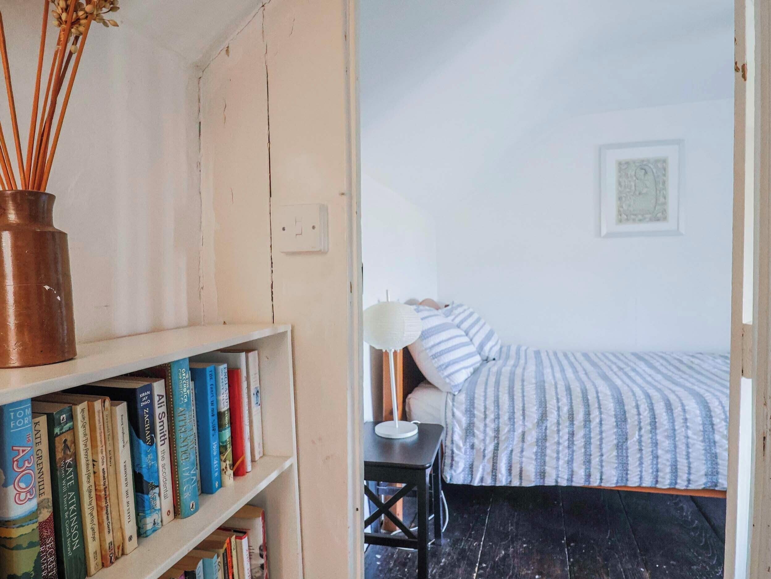 Um quarto com uma cama, uma mesa de cabeceira, um abajur e uma estante com livros.