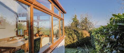 A room with a large window, a wooden table, and a view of a garden.