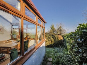 A room with a large window, a wooden table, and a view of a garden. - 2 Oak Tree Cottages (Axminster)