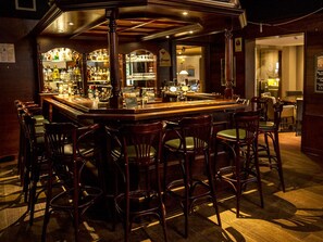 A bar area with wooden bar stools, a bar counter, and a variety of bottles and glasses.