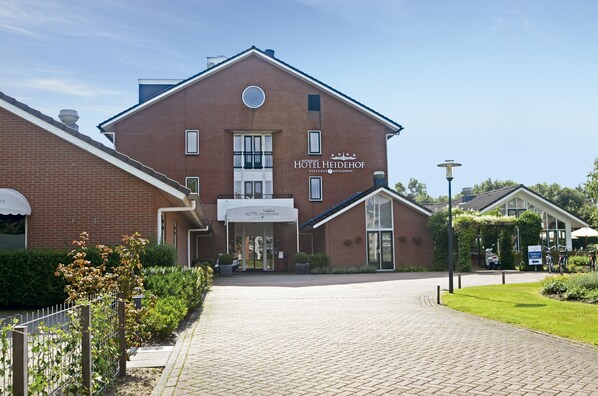 A hotel with a brick facade, a sign reading 'HOTEL HEIDEHOF,' and a paved entrance.