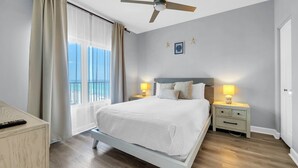 A hotel room with a bed, two bedside tables, a ceiling fan, a window with curtains, and a view of the beach. - 🌊Large Balcony-Gulf Views-Multiple Pools-Shores of Panama 925🌊 (Panama City Beach)