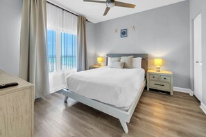 A hotel room with a bed, two bedside tables, a ceiling fan, a window with curtains, and a view of the beach. - 🌊Large Balcony-Gulf Views-Multiple Pools-Shores of Panama 925🌊 (Panama City Beach)