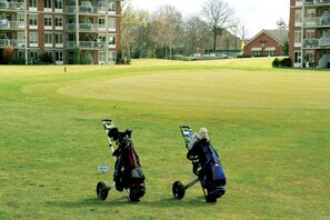 Un terrain de golf avec deux voiturettes, un panneau indiquant la présence d’un chariot, et un hôtel en arrière-plan.