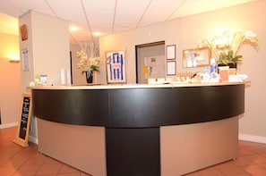 Un comptoir d’accueil aux couleurs noir et beige, des tableaux encadrés accrochés au mur et une plante en pot.