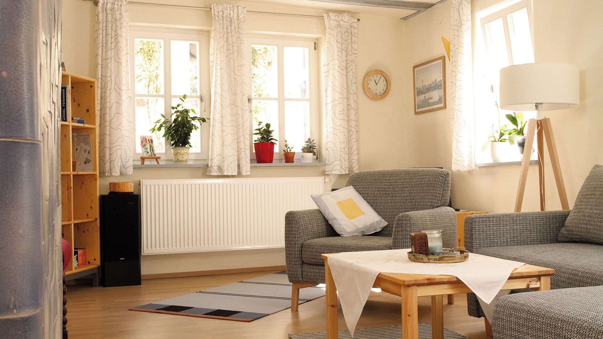 Ein gemütliches Wohnzimmer mit einer Couch, einem kleinen Tisch, einem Bücherregal, einer Heizung und einem Fenster mit Vorhängen.