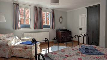 Ein Schlafzimmer mit Bett, Sofa, Schminktisch und Heizkörper, sowie einem Fenster mit Vorhängen.