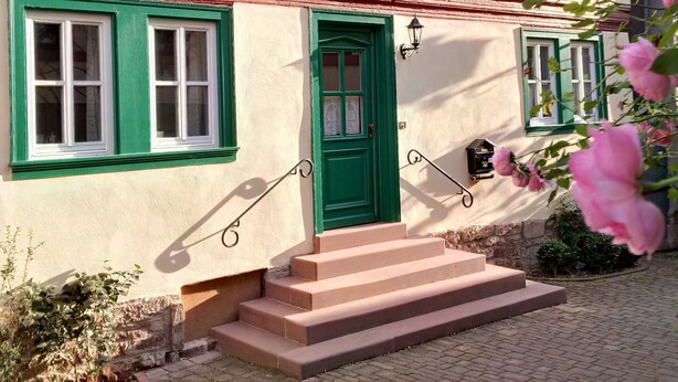 A building with a green door, multiple windows with green frames, and a small garden area with steps leading to the entrance. - Historic wine farmhouse in Main/Wine Franconia at the foot of the Spessart (Triefenstein)