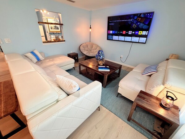 A living room with a sofa set, a coffee table, a lamp, a TV mounted on the wall, and a small side table.