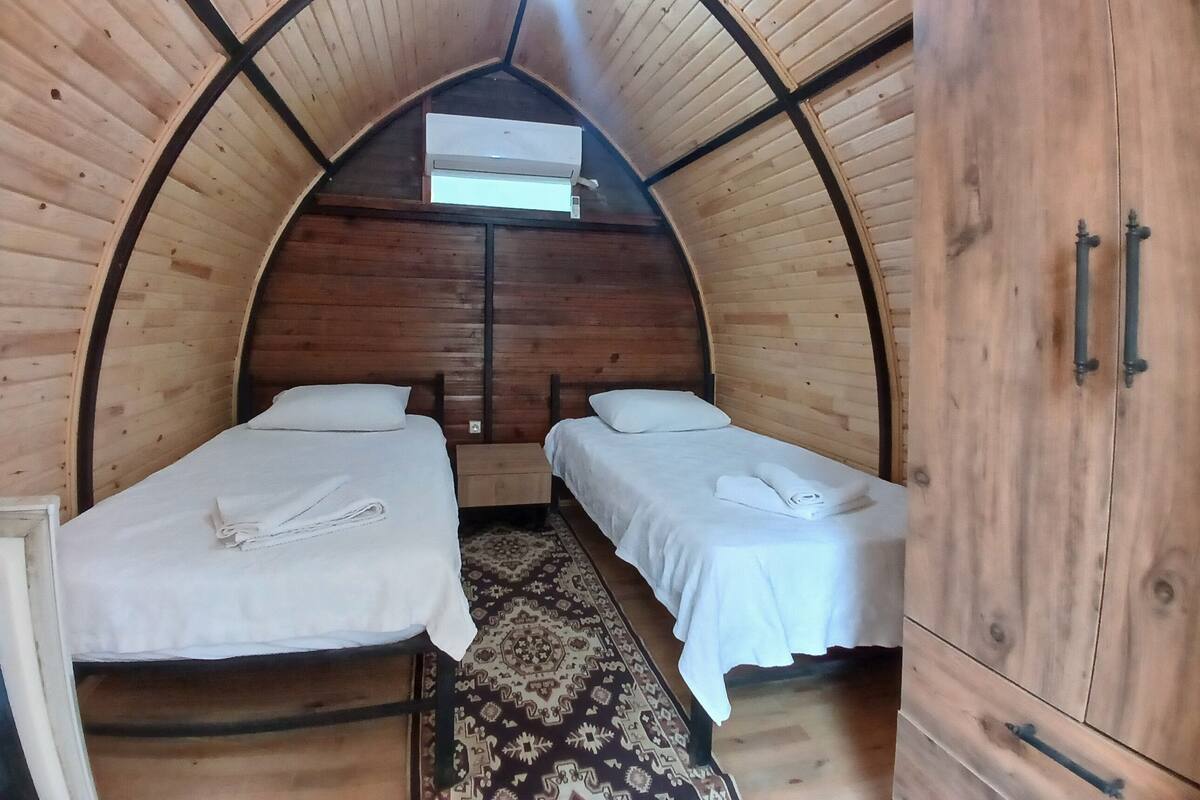 A cozy, arched wooden room with two beds, a wardrobe, and a ceiling fan.