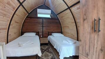 Una habitación acogedora de madera con arco, con dos camas, un armario y un ventilador de techo.