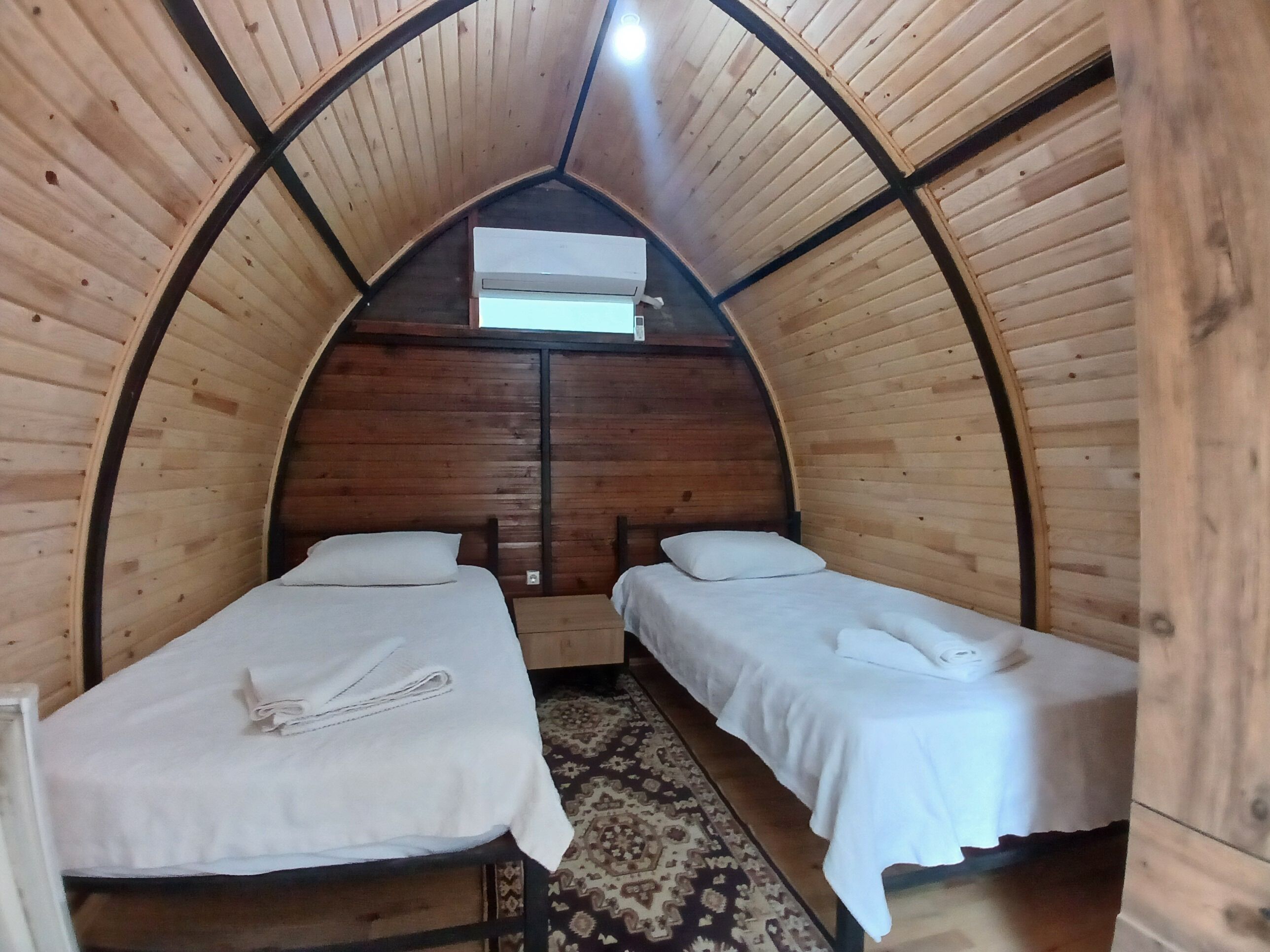 Una habitación acogedora de madera con arco, con dos camas, una alfombra estampada y un ventanal en lo alto.