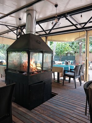 Un patio al aire libre con estufa de leña, mobiliario exterior y vistas a una piscina.