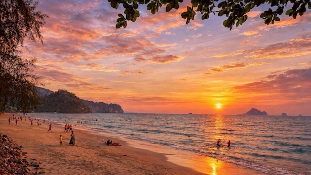 Ein Strand mit Menschen, einem Sonnenuntergang und fernen Inseln.