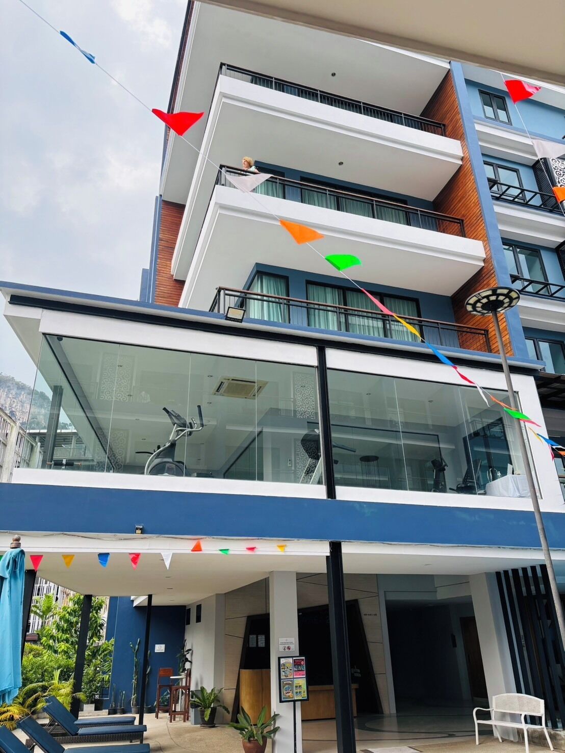 Un hotel de varios pisos con fachada de vidrio, mesas al aire libre y un balcón.