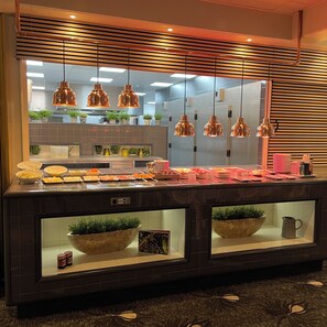 A buffet area with a variety of food items, hanging pendant lights, and potted plants.