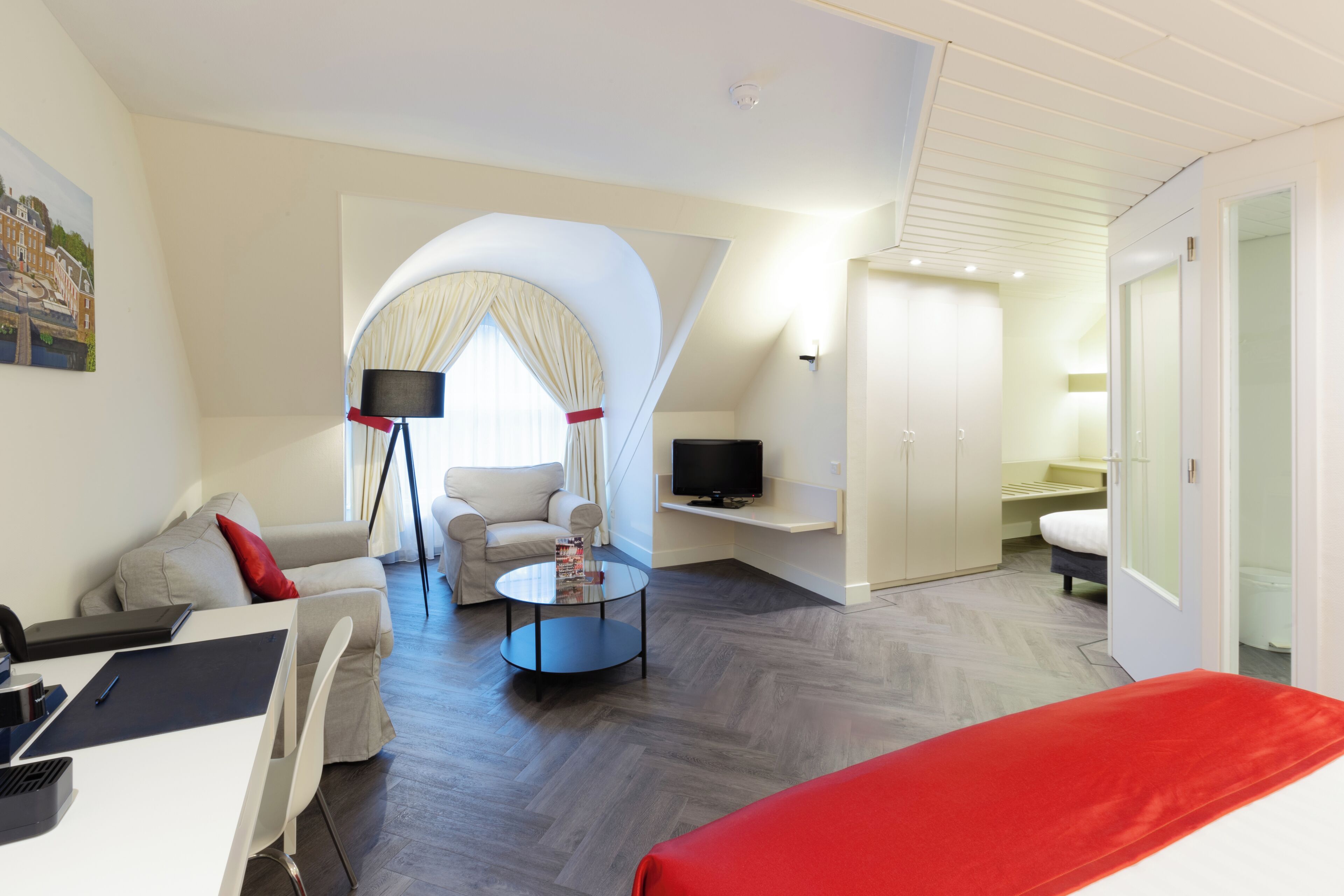 A modern hotel room with a sofa, armchair, TV, and a small table.
