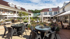 An outdoor patio area with round tables and wicker chairs, surrounded by buildings with red-tiled roofs and large windows. - Unwind in Zeist with On-site Pool, Dining, Free Parking, and a Peaceful Ambiance (Zeist)