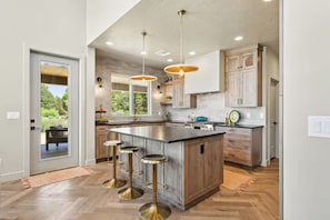 A modern kitchen with a large island, bar stools, pendant lights, and wooden cabinetry. - New Zion cabin with hot tub, sauna, cold plunge @ Zion Knotty Pines (Mount carmel)