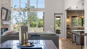 Eine moderne Küche mit großem Fenster, ein Essbereich mit Tisch für zwei Personen und eine gemütliche Sitzecke mit Blick ins Freie.