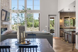 A modern kitchen with a large window, a dining area with a table set for two, and a cozy seating area with a view of the outdoors. - New Zion cabin with hot tub, sauna, cold plunge @ Zion Knotty Pines (Mount carmel)